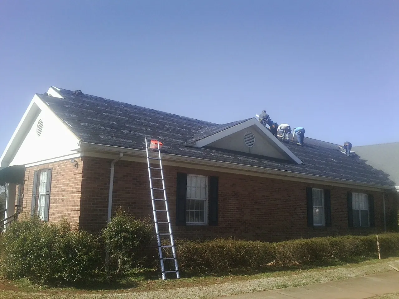 Crew tearing shingles off a brick ranch roof with a ladder set — Metal Roof Repair work by our crew in Port Trevorton
