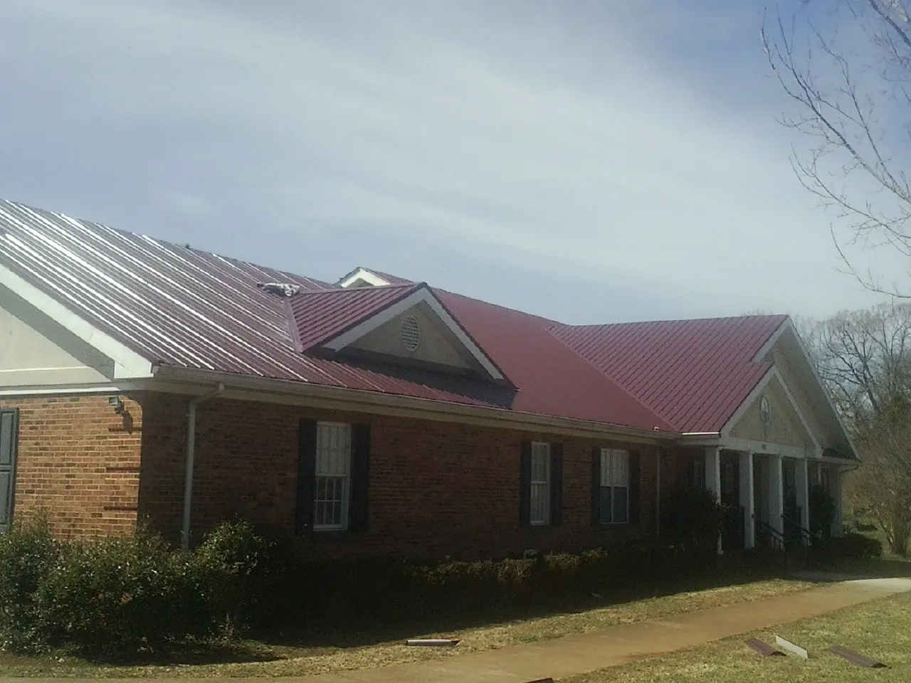 Red metal roof with gabled entries on a long brick building, from a Hail Damage Roof Repair job in Port Trevorton