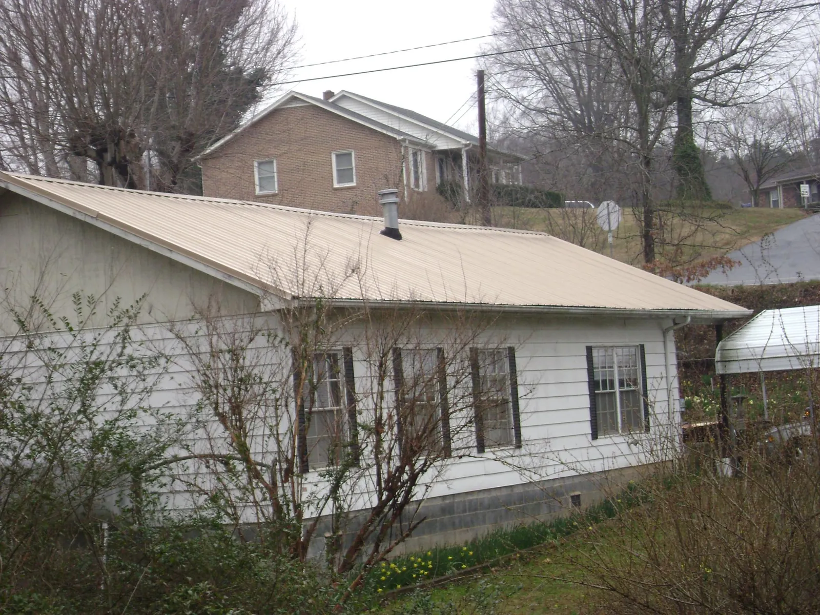 Tan metal roof on a white sided house set into a hillside — Commercial Roofing by Roofing Brothers in Port Trevorton